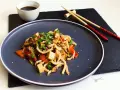 Pyszne udon z tofu, warzywami i sezamem, podane na ciemnym talerzu z pałeczkami.