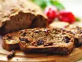 Pokrojony niskokaloryczny chlebek bananowy z kawałkami czekolady i rodzynkami, na drewnianej desce, w tle czerwone kwiaty.