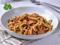 Pyszne udon z kurczakiem i warzywami, posypane świeżą natką pietruszki.