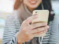 Uśmiechnięta osoba trzymająca złoty smartfon z podłączonymi słuchawkami dousznymi. Czy słuchawki douszne są szkodliwe?