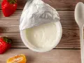 Jogurt naturalny właściwości: kremowy, gładki, z owocami i łyżeczką na drewnianym tle. Idealny na zdrowy deser.