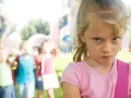 Zmarszczona mina 7-latki, która wydaje się być zirytowana. W tle inne dzieci, być może świadkowie jej niepokojących zachowań.