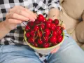 Ręce trzymają miseczkę pełną soczystych, czerwonych czeresni. Idealna przekąska na keto!