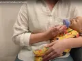 Instrukcja jak prawidłowo karmić butelką niemowlę. Pokazano karmienie lalki-niemowlaka.
