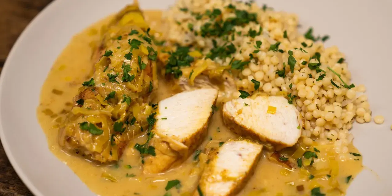 Pyszne curry z kurczakiem w kremowym sosie, podane z kaszą kuskus i posypane natką pietruszki.