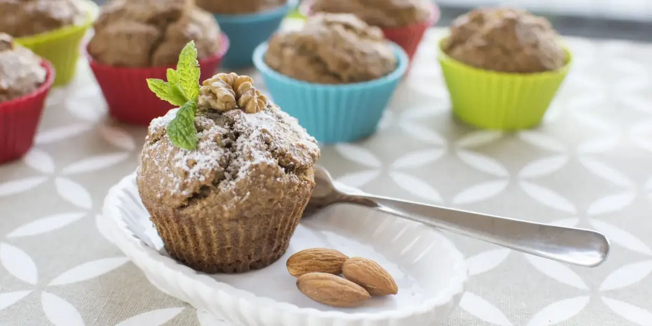 Pyszne muffinki bananowe fit, udekorowane miętą i orzechami, na talerzyku z migdałami.