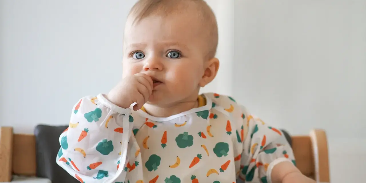 Niebieskooki maluch w śliniaczku z marchewkami i bananami, kiedy dziecko widzi kolory.