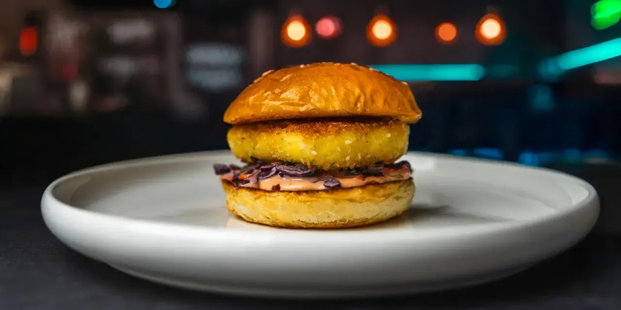 Apetyczny burger z halloumi, z chrupiącą panierką i kolorową surówką, na białym talerzu.