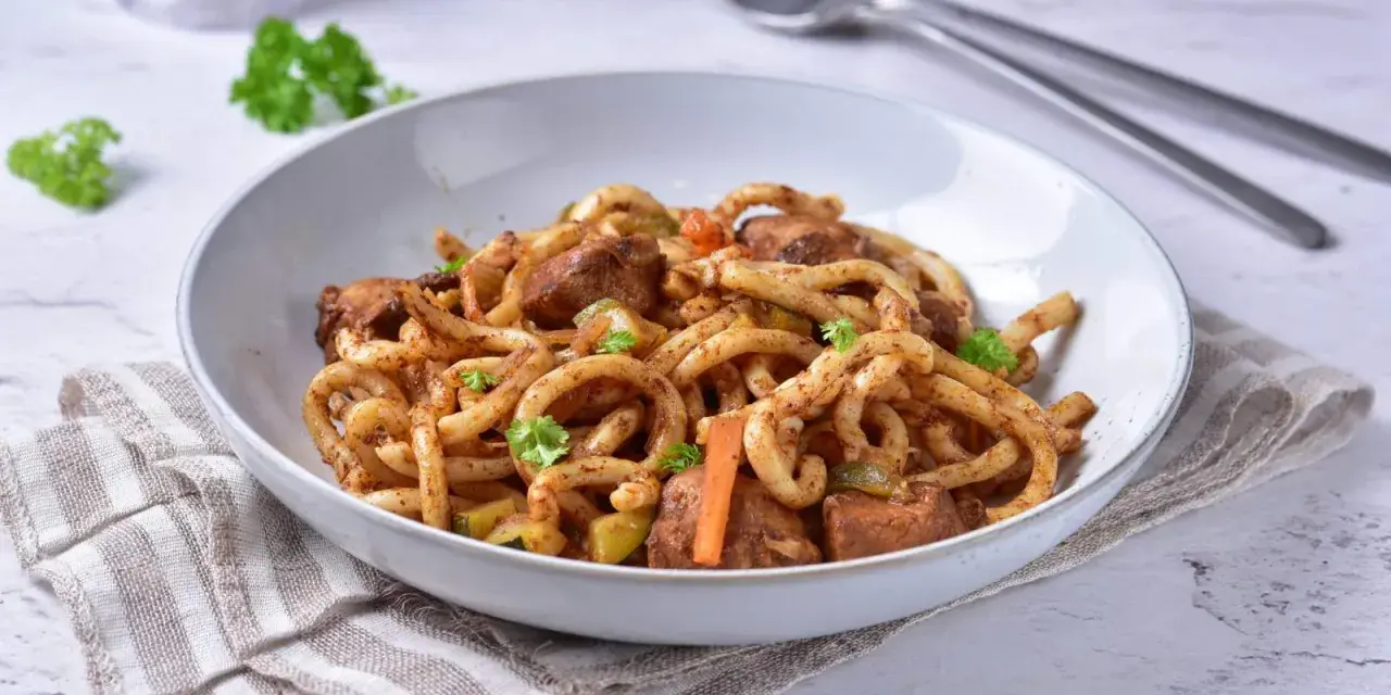 Pyszne udon z kurczakiem i warzywami, posypane świeżą natką pietruszki.