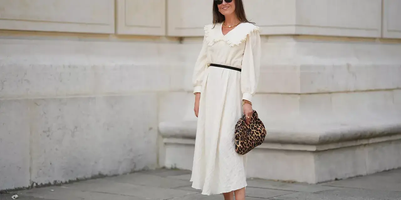 Kobieta w kremowej sukience z falbankowym kołnierzem, czarnym paskiem i panterkową kopertówką. Uosobienie swobodnej elegancji smart casual damski.