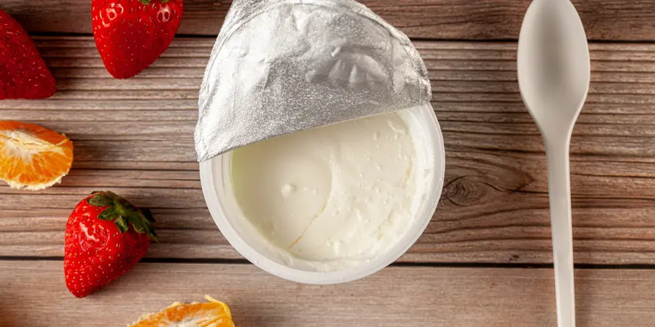 Jogurt naturalny właściwości: kremowy, gładki, z owocami i łyżeczką na drewnianym tle. Idealny na zdrowy deser.
