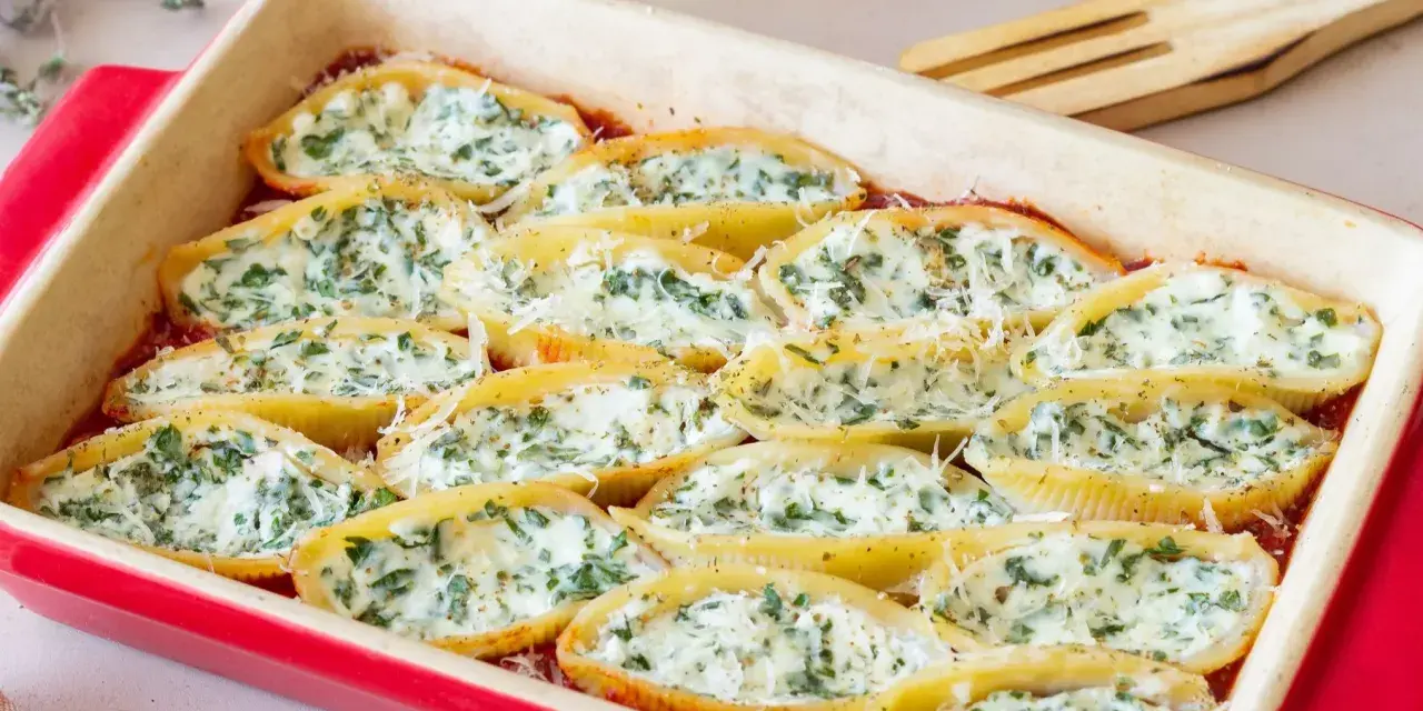 Pyszne muszle ze szpinakiem i ricottą, zapieczone w sosie pomidorowym, posypane parmezanem.