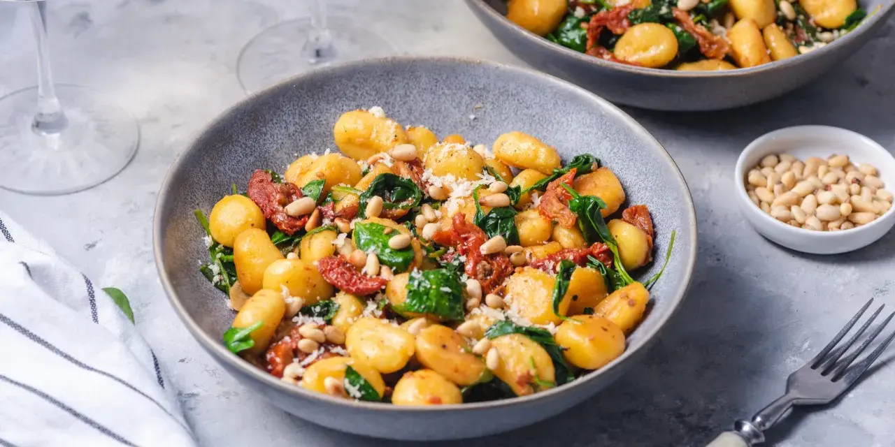 Pyszne gnocchi z pomidorami, szpinakiem i orzeszkami pinii, posypane parmezanem. Idealne danie na szybki obiad.