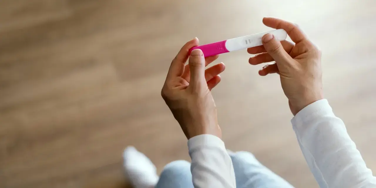 Dłonie trzymające test ciążowy, który może wskazać pierwsze objawy ciąży.