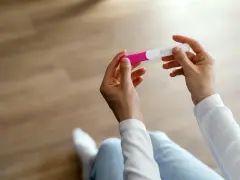 Dłonie trzymające test ciążowy, który może wskazać pierwsze objawy ciąży.