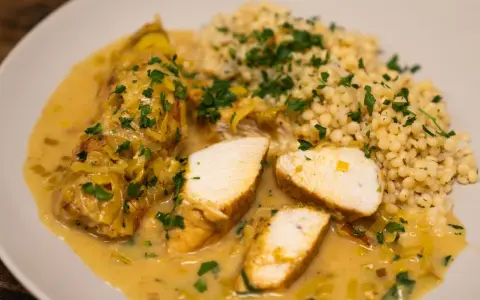Pyszne curry z kurczakiem w kremowym sosie, podane z kaszą kuskus i posypane natką pietruszki.
