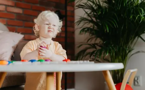 Mały chłopiec z miną wyrażającą bunt 4 latka objawy, trzyma w rączkach fioletową zabawkę.