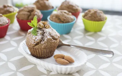 Pyszne muffinki bananowe fit, udekorowane miętą i orzechami, na talerzyku z migdałami.