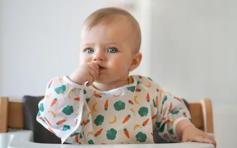 Niebieskooki maluch w śliniaczku z marchewkami i bananami, kiedy dziecko widzi kolory.