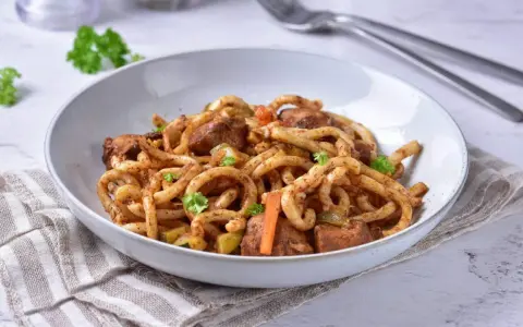 Pyszne udon z kurczakiem i warzywami, posypane świeżą natką pietruszki.