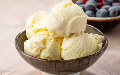 Pyszne, kremowe lody waniliowe w miseczce. Idealne na deser, pokazują, jak się robi lody. W tle owoce.