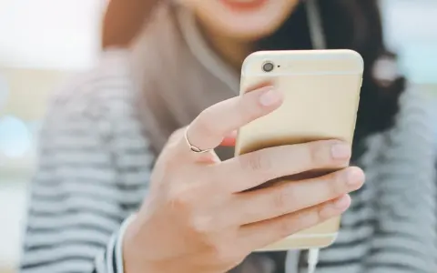 Uśmiechnięta osoba trzymająca złoty smartfon z podłączonymi słuchawkami dousznymi. Czy słuchawki douszne są szkodliwe?