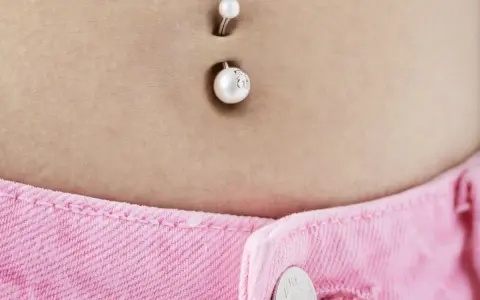 Kolczyk w pępku, ozdobiony perłami. Wiele osób zastanawia się, od ilu lat można mieć kolczyk w pępku, by wyglądać stylowo.