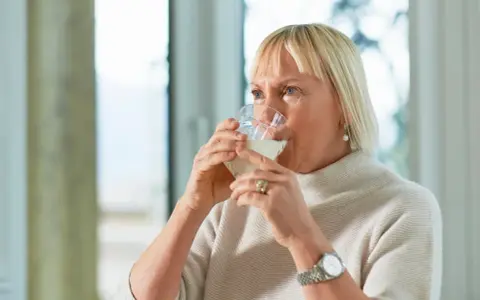 Kobieta pije wodę, szukając sposobu, jak pozbyć się wody z organizmu.