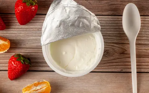 Jogurt naturalny właściwości: kremowy, gładki, z owocami i łyżeczką na drewnianym tle. Idealny na zdrowy deser.