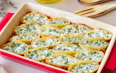 Pyszne muszle ze szpinakiem i ricottą, zapieczone w sosie pomidorowym, posypane parmezanem.