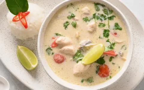 Aromatyczna tajska zupa z kurczakiem, podana z ryżem, limonką i chili.