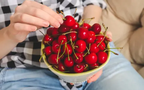 Ręce trzymają miseczkę pełną soczystych, czerwonych czeresni. Idealna przekąska na keto!