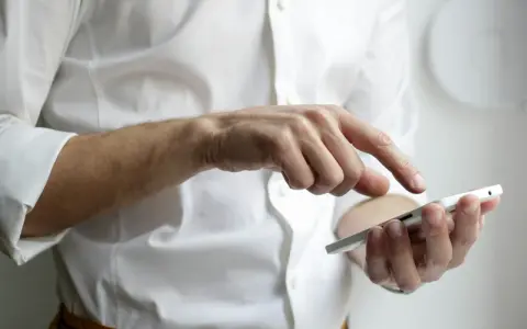 Mężczyzna w białej koszuli używa smartfona, czując narastający ból głowy od telefonu.