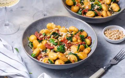 Pyszne gnocchi z pomidorami, szpinakiem i orzeszkami pinii, posypane parmezanem. Idealne danie na szybki obiad.