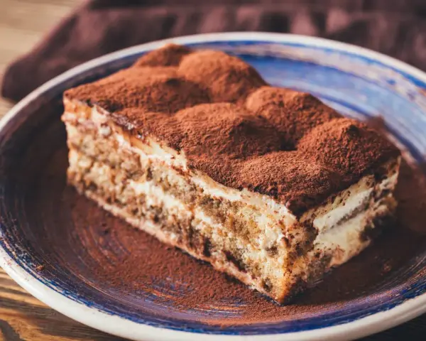 Pyszne tiramisu ze skyrem, posypane kakao, na niebieskim talerzu. Idealne na deser.