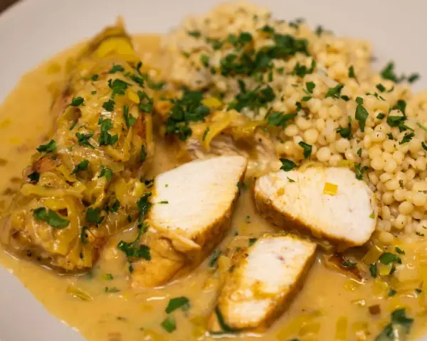 Pyszne curry z kurczakiem w kremowym sosie, podane z kaszą kuskus i posypane natką pietruszki.