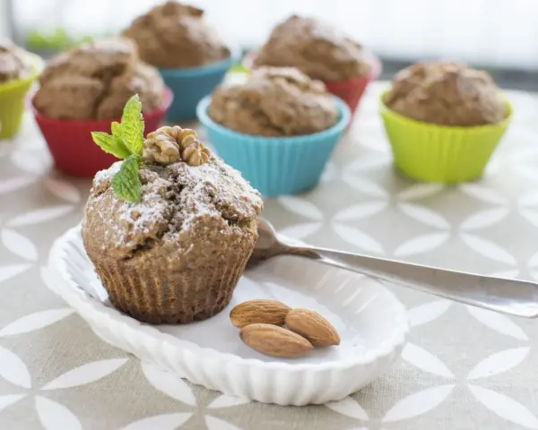 Pyszne muffinki bananowe fit, udekorowane miętą i orzechami, na talerzyku z migdałami.
