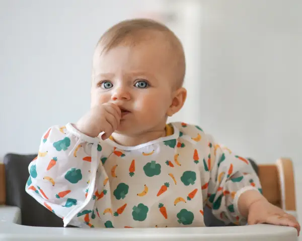 Niebieskooki maluch w śliniaczku z marchewkami i bananami, kiedy dziecko widzi kolory.