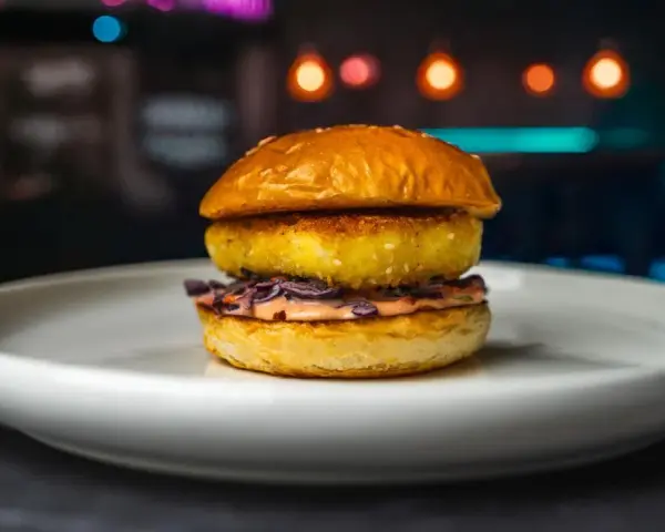 Apetyczny burger z halloumi, z chrupiącą panierką i kolorową surówką, na białym talerzu.