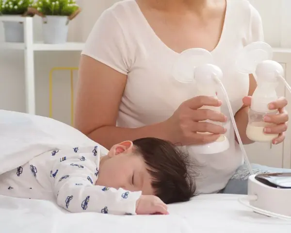 Mama odciąga pokarm 7-5-3, podczas gdy jej dziecko śpi spokojnie.