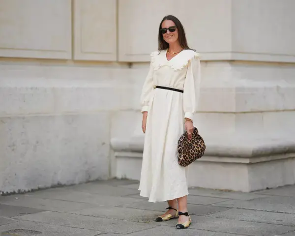 Kobieta w kremowej sukience z falbankowym kołnierzem, czarnym paskiem i panterkową kopertówką. Uosobienie swobodnej elegancji smart casual damski.