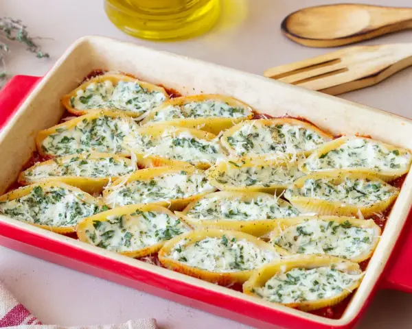 Pyszne muszle ze szpinakiem i ricottą, zapieczone w sosie pomidorowym, posypane parmezanem.