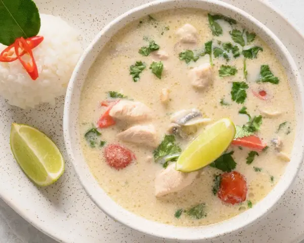Aromatyczna tajska zupa z kurczakiem, podana z ryżem, limonką i chili.
