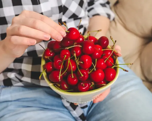 Ręce trzymają miseczkę pełną soczystych, czerwonych czeresni. Idealna przekąska na keto!
