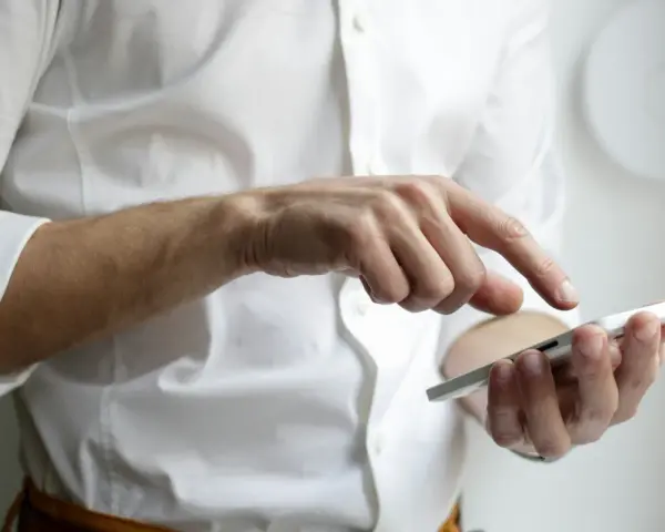 Mężczyzna w białej koszuli używa smartfona, czując narastający ból głowy od telefonu.