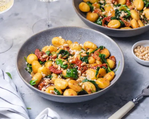 Pyszne gnocchi z pomidorami, szpinakiem i orzeszkami pinii, posypane parmezanem. Idealne danie na szybki obiad.