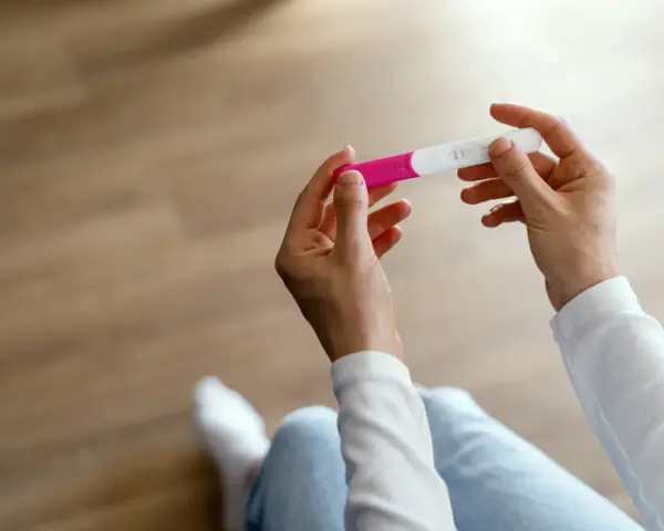 Dłonie trzymające test ciążowy, który może wskazać pierwsze objawy ciąży.