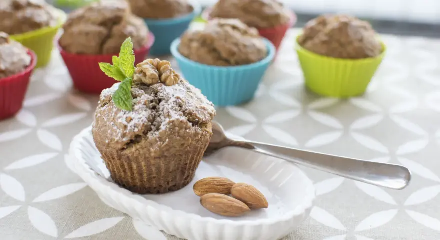 Pyszne muffinki bananowe fit, udekorowane miętą i orzechami, na talerzyku z migdałami.