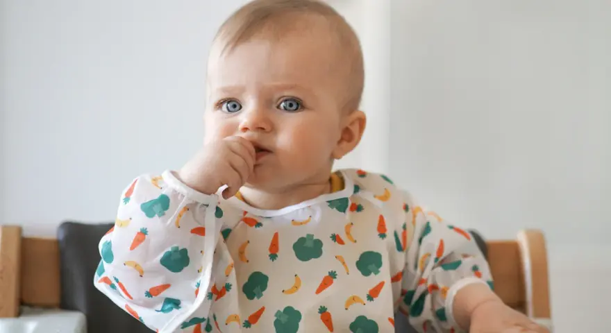 Niebieskooki maluch w śliniaczku z marchewkami i bananami, kiedy dziecko widzi kolory.