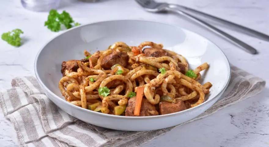 Pyszne udon z kurczakiem i warzywami, posypane świeżą natką pietruszki.